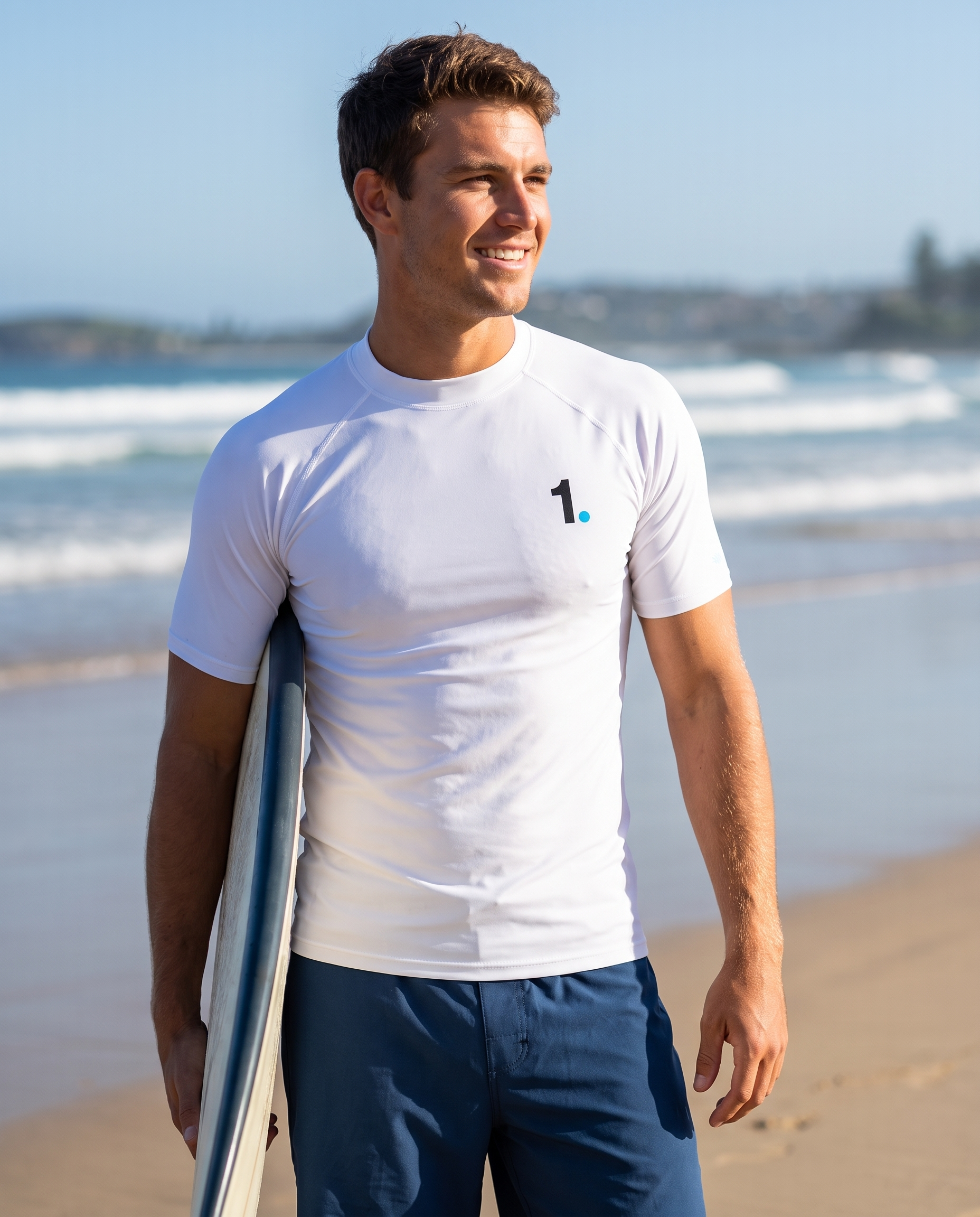 Man wearing Base1 Logo rash guard with a surfboard on the beach
